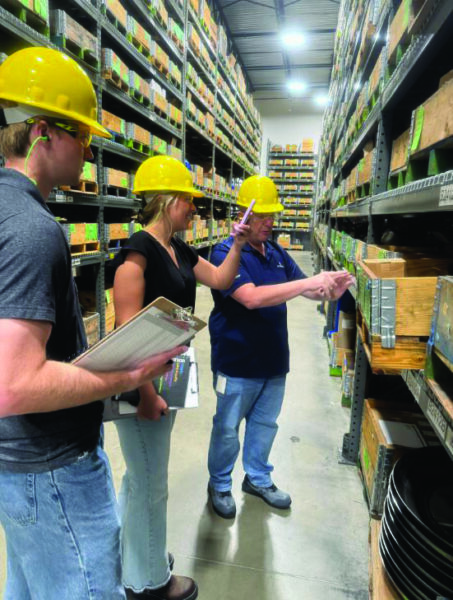 Tauber students on the 2025 Emerson project team collaborating with a company employee in a warehouse, assessing inventory and supply chain operations.