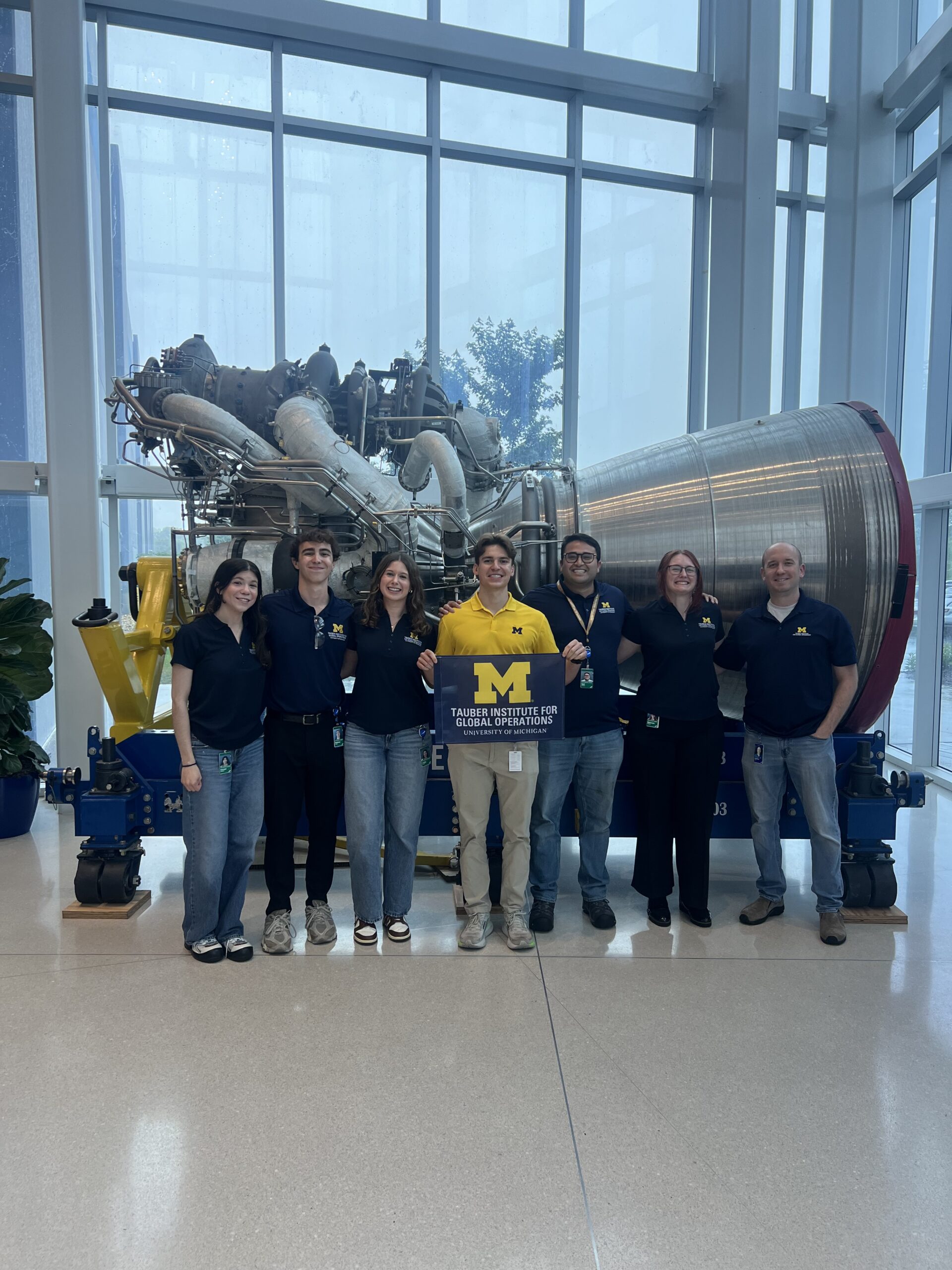 A group of people holding a flag in front of aerospace equipment.