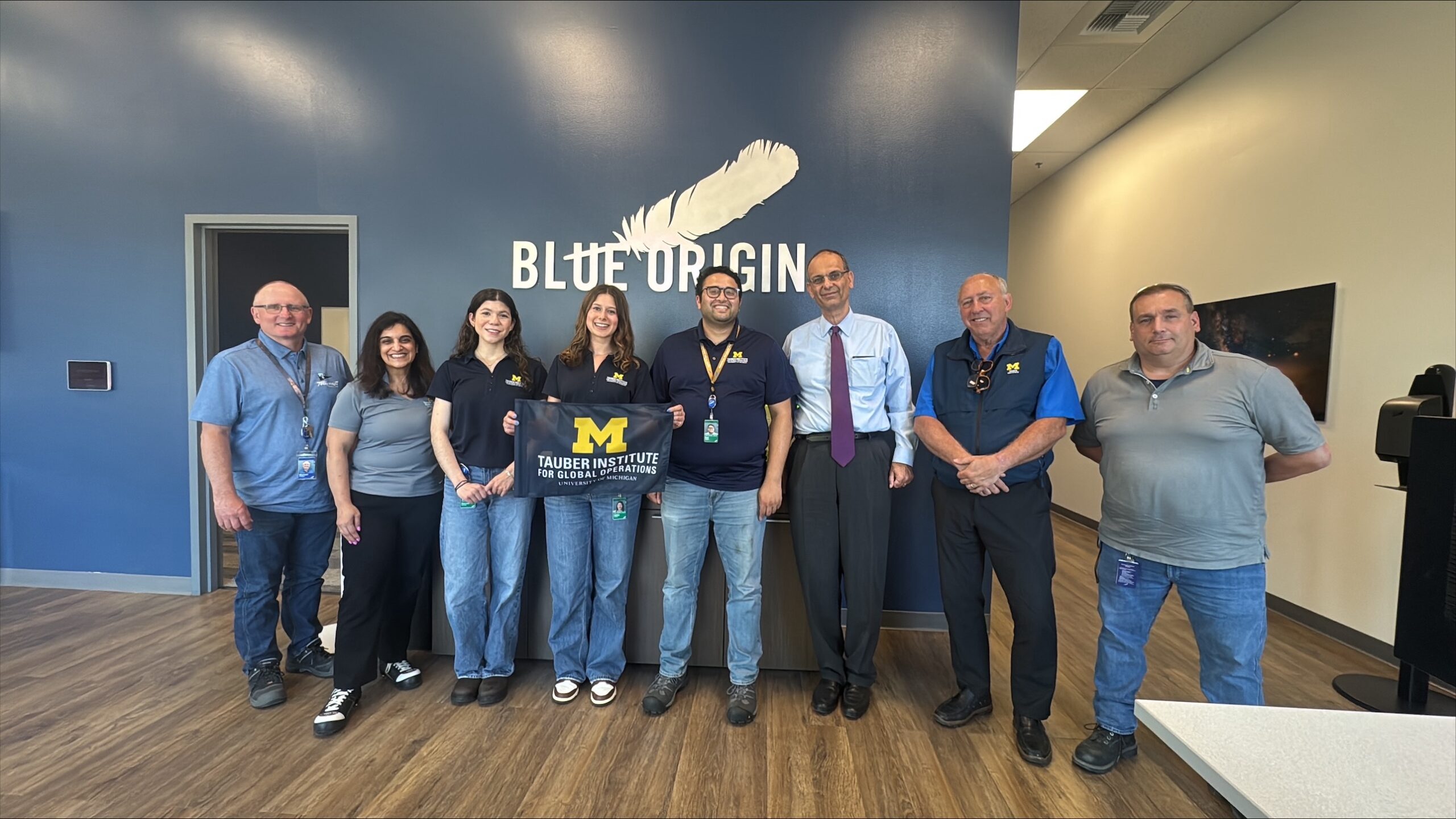 A group of people holding a flag in front of the Blue Origin logo