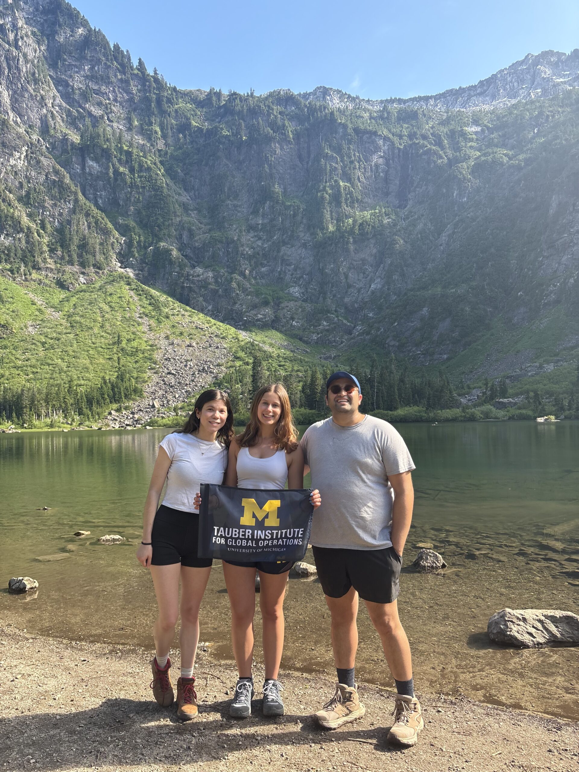 Three students holding a flag in front of a mountain range