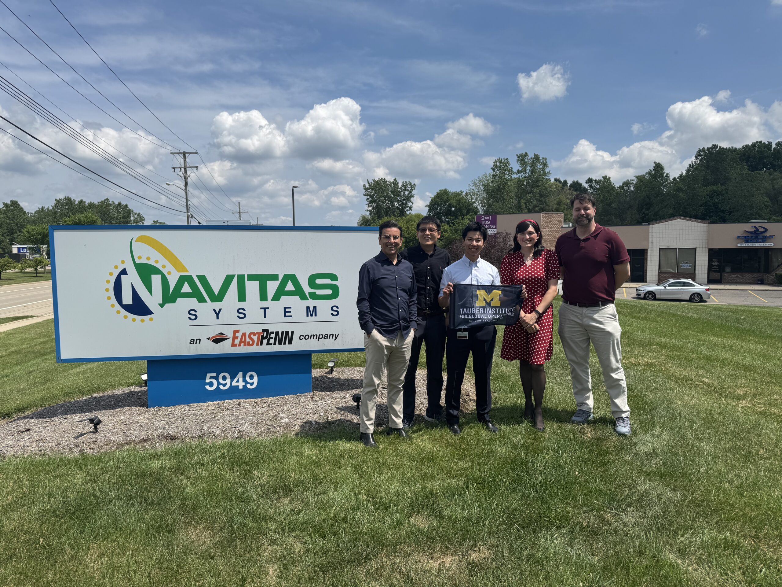 A group of people posing in front of the Navitas sign