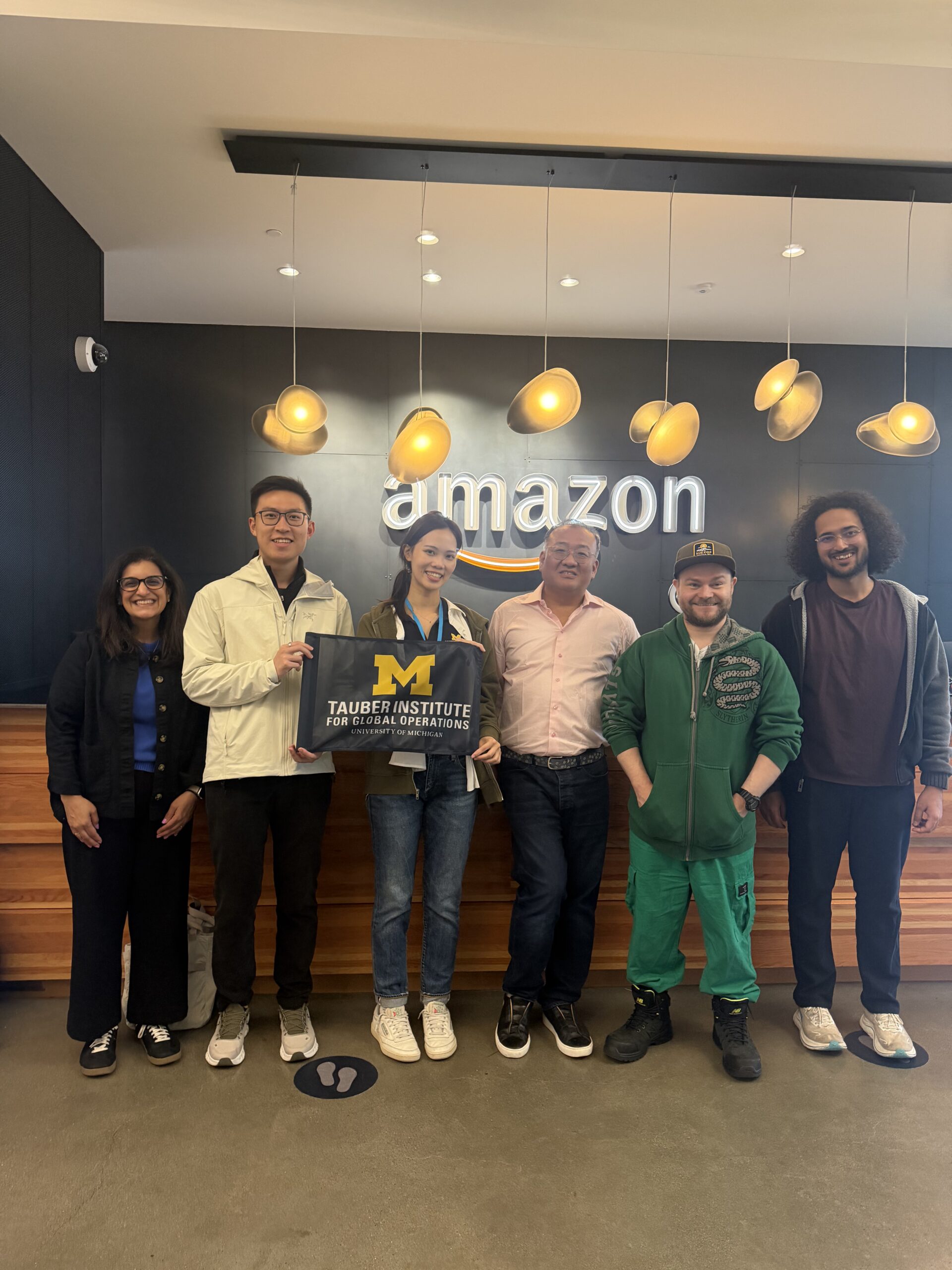A group poses in front of the amazon logo holding the Tauber flag.