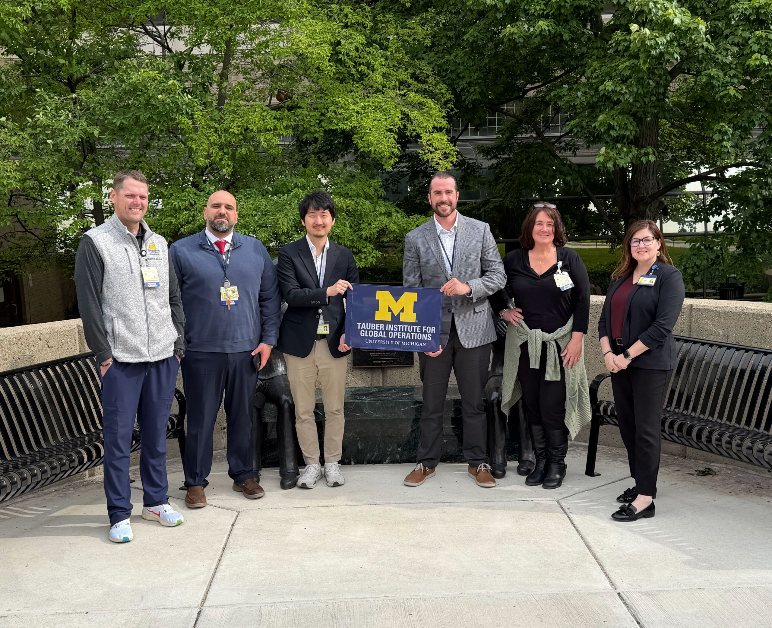 A group of Michigan Medicine employees pose with the Tauber Flag in front of a building