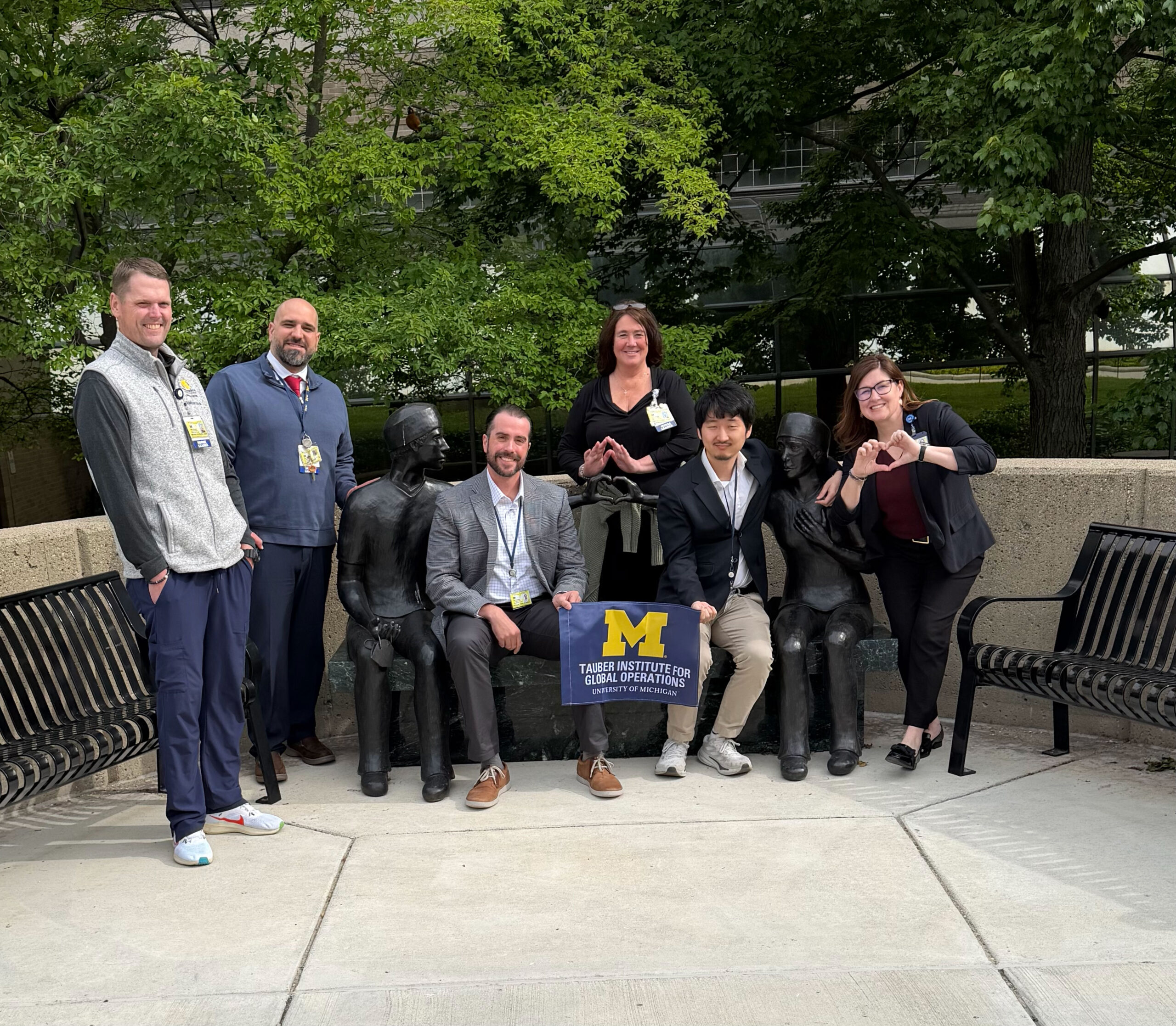 A group of Michigan Medicine employees pose in front of a building with the Tauber Flag