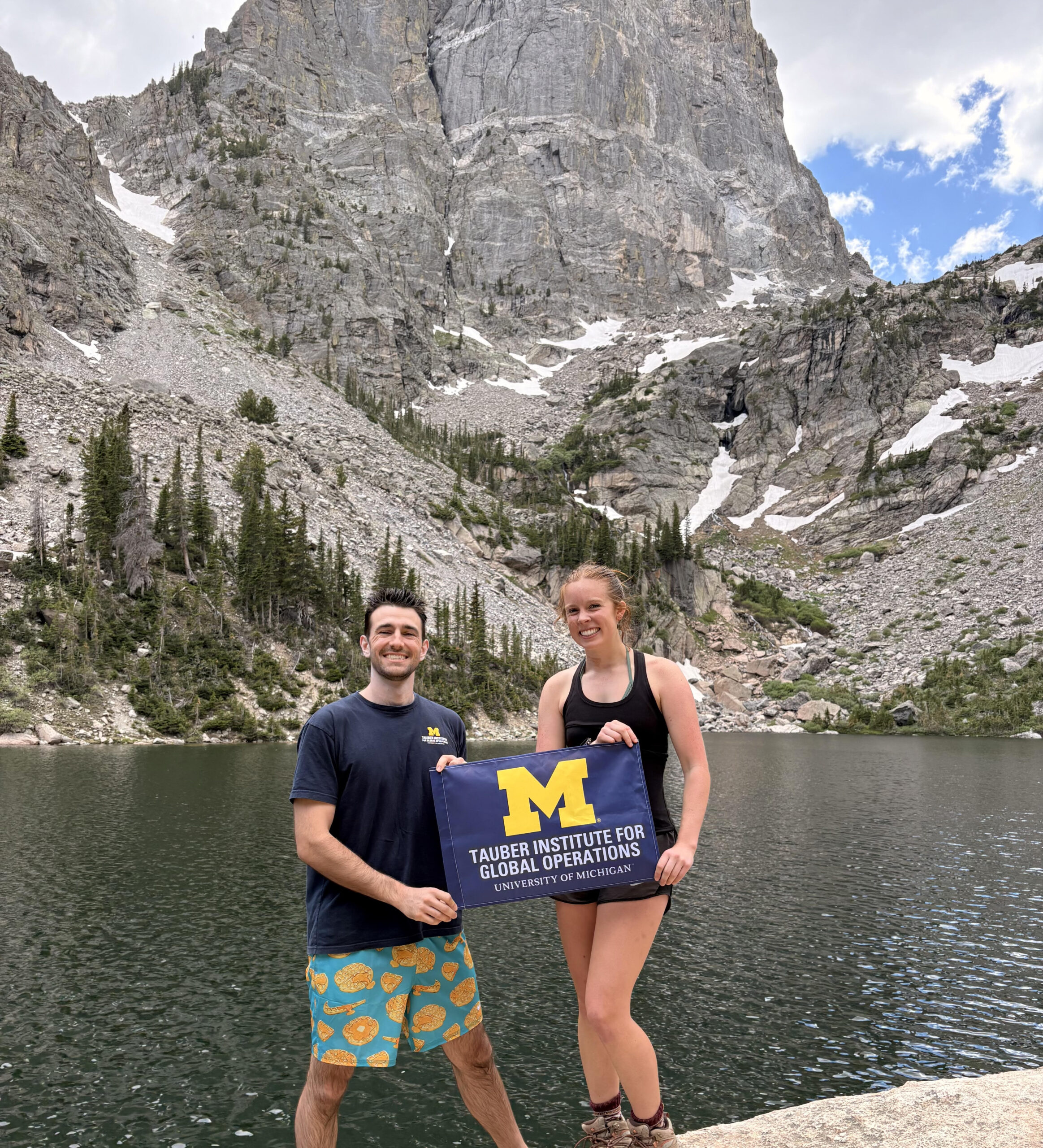 A male and female student hold a flag in front of mountains.