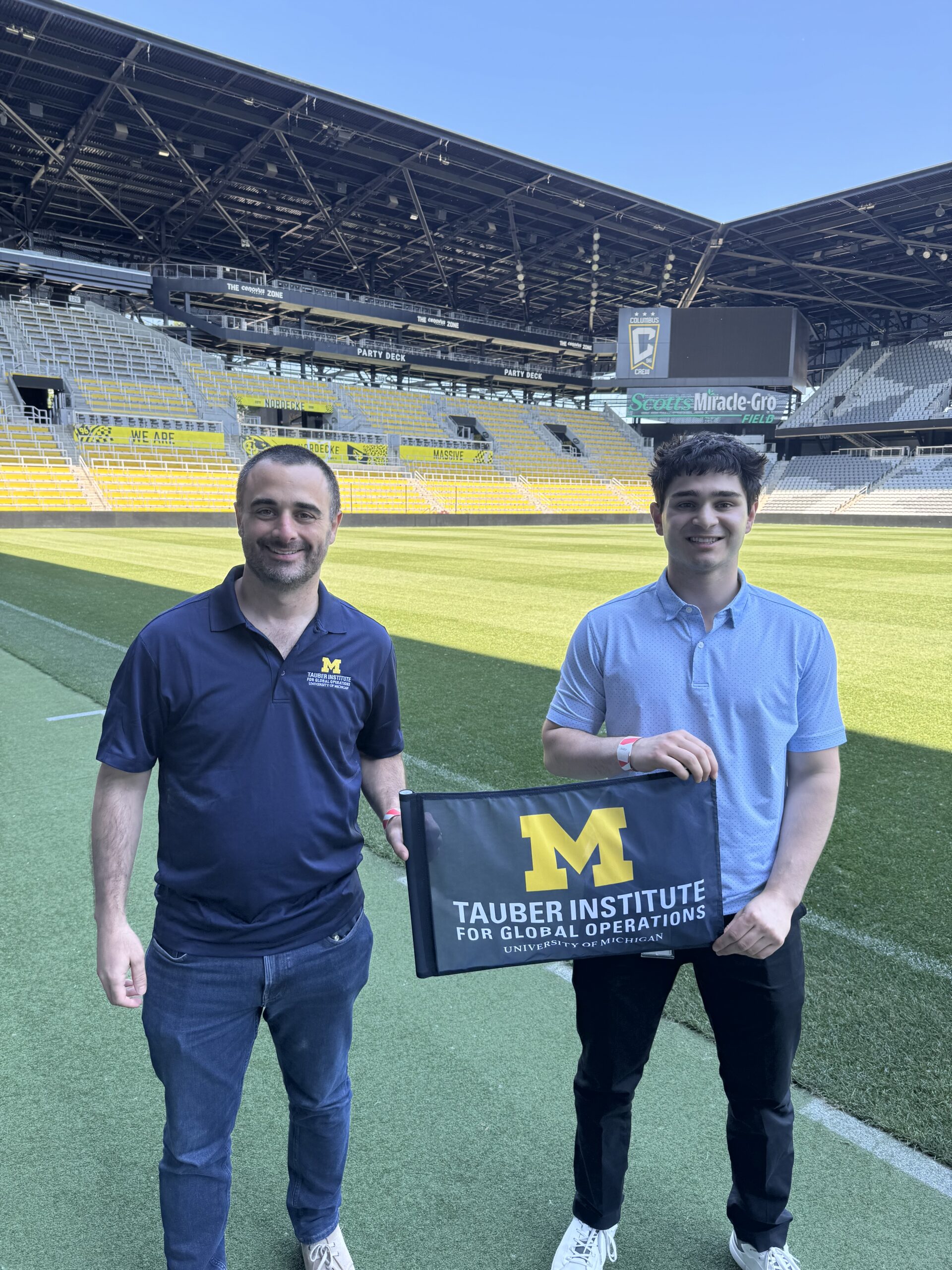 Two students pose on a soccer pitch with the Tauber Flag
