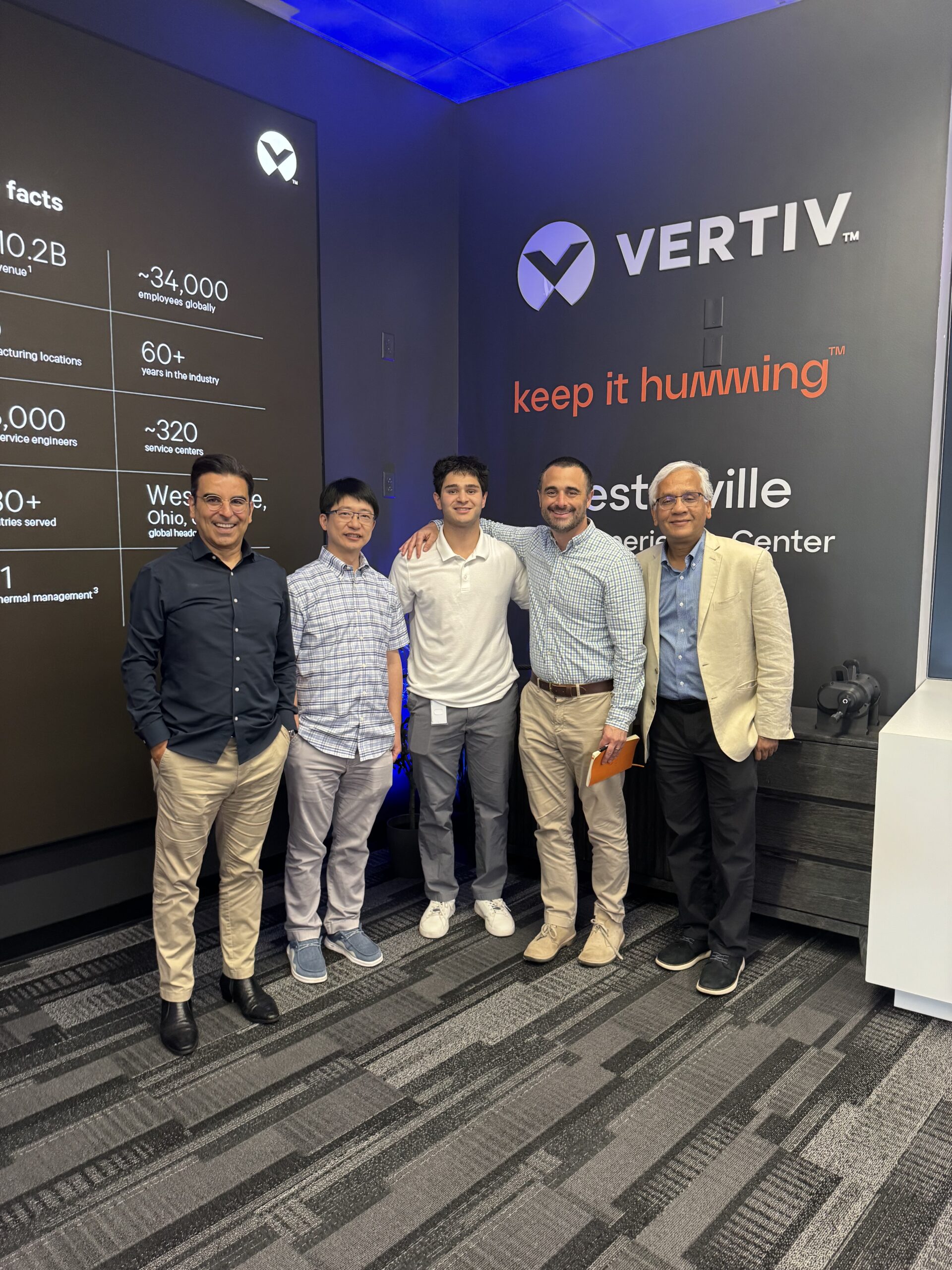 A group of people pose in front of the Vertiv logo