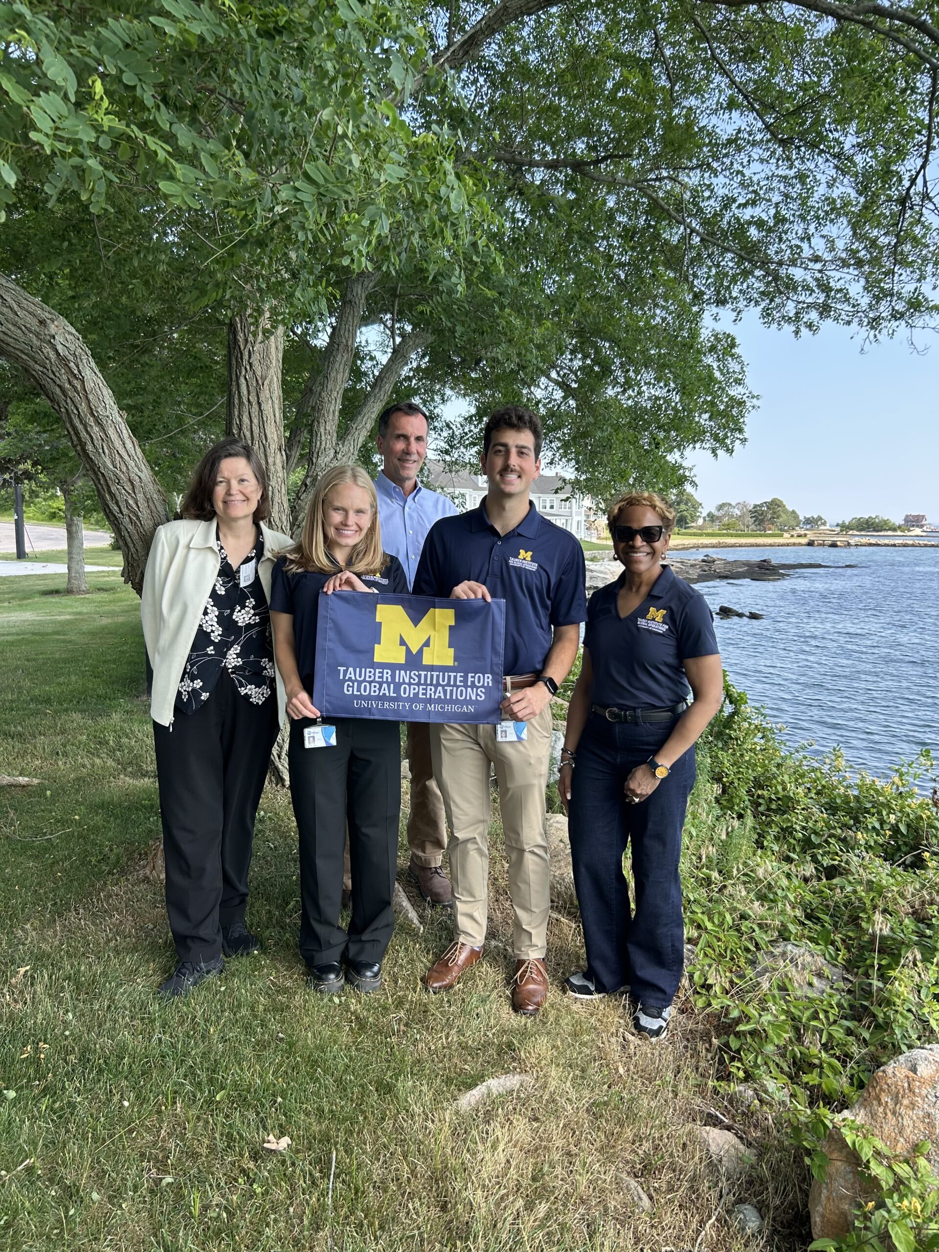 A group of people holding the tauber flag in front of a tree and water